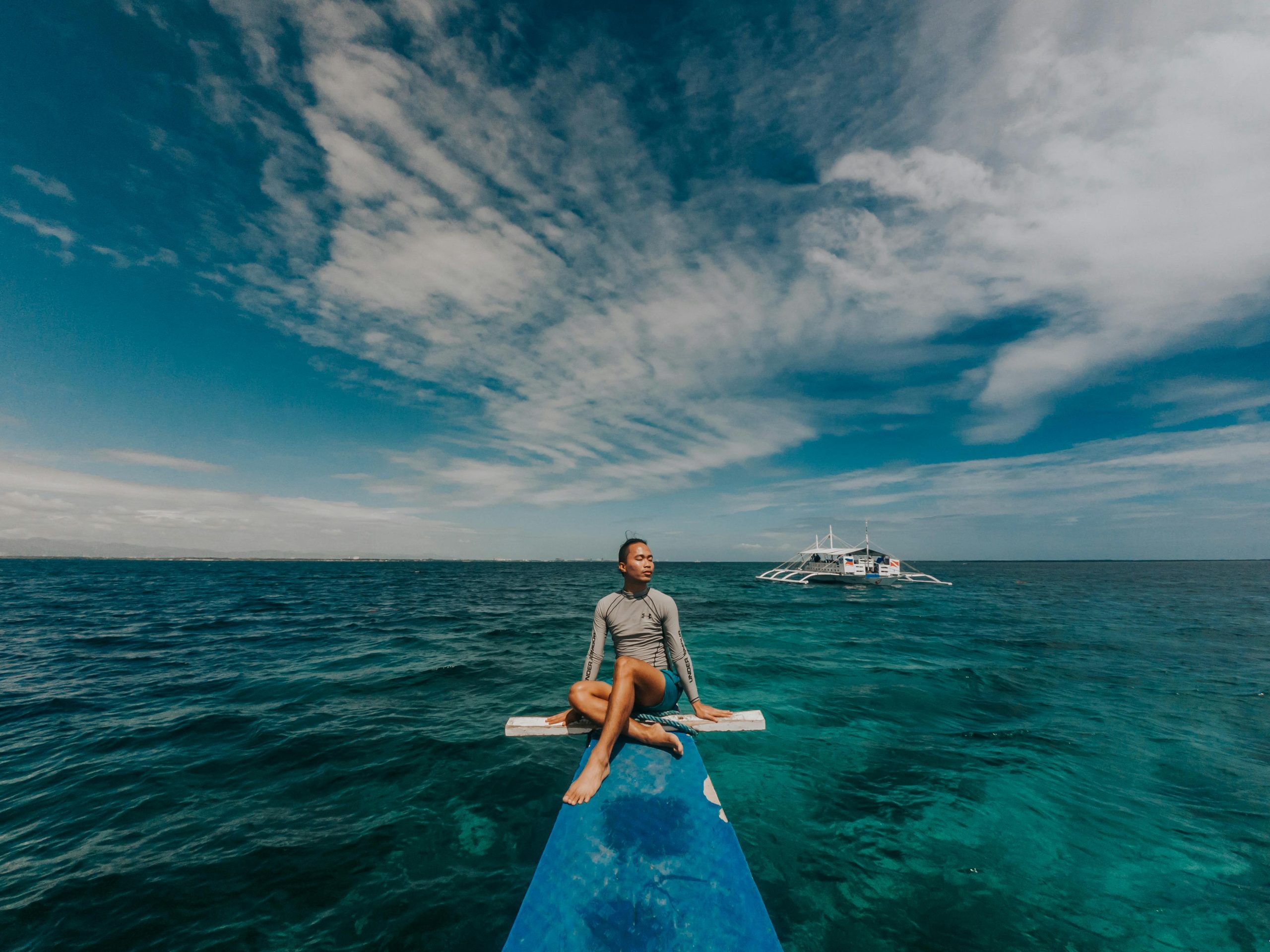 Man sitting on a boat's bow, enjoying a peaceful ocean view under a blue sky.